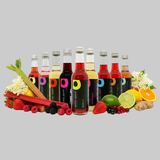 Nine bottles of various colored cordials arranged in a line against a white background.