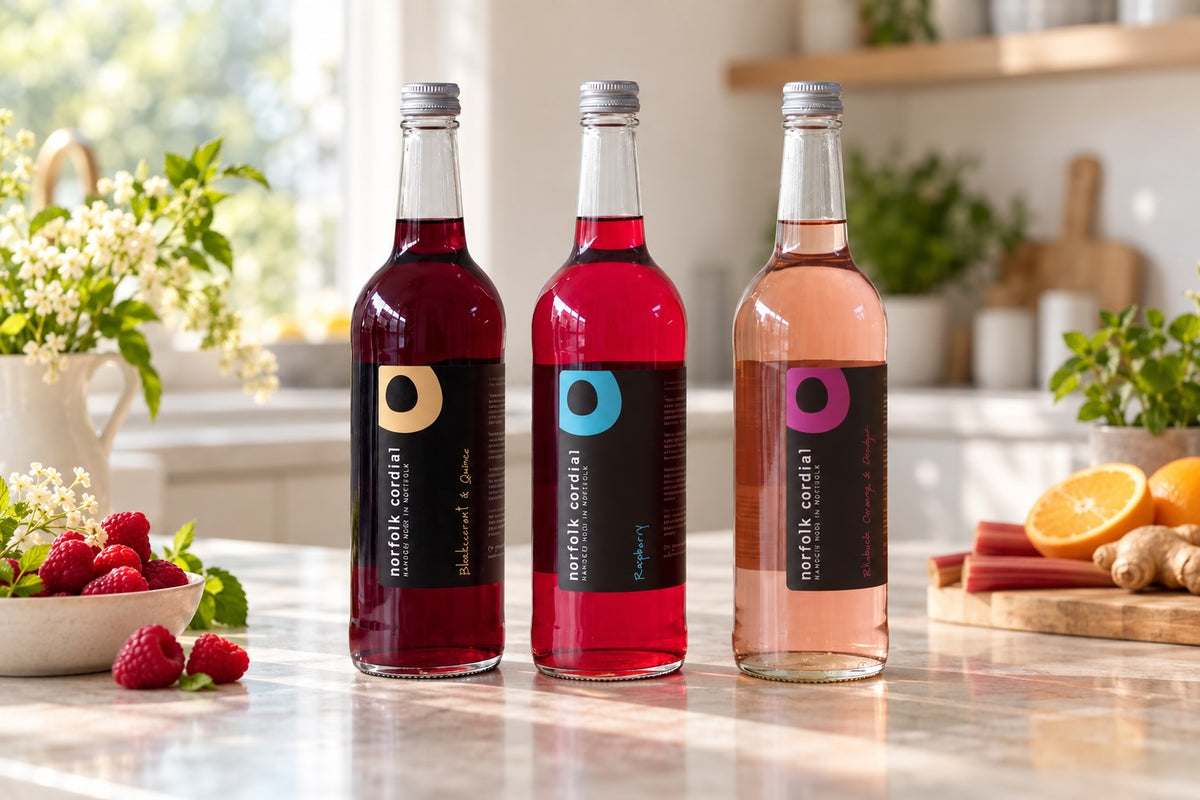 Three 750ml Norfolk Cordial bottles in assorted flavours displayed on a pale stone worktop in a bright contemporary kitchen.