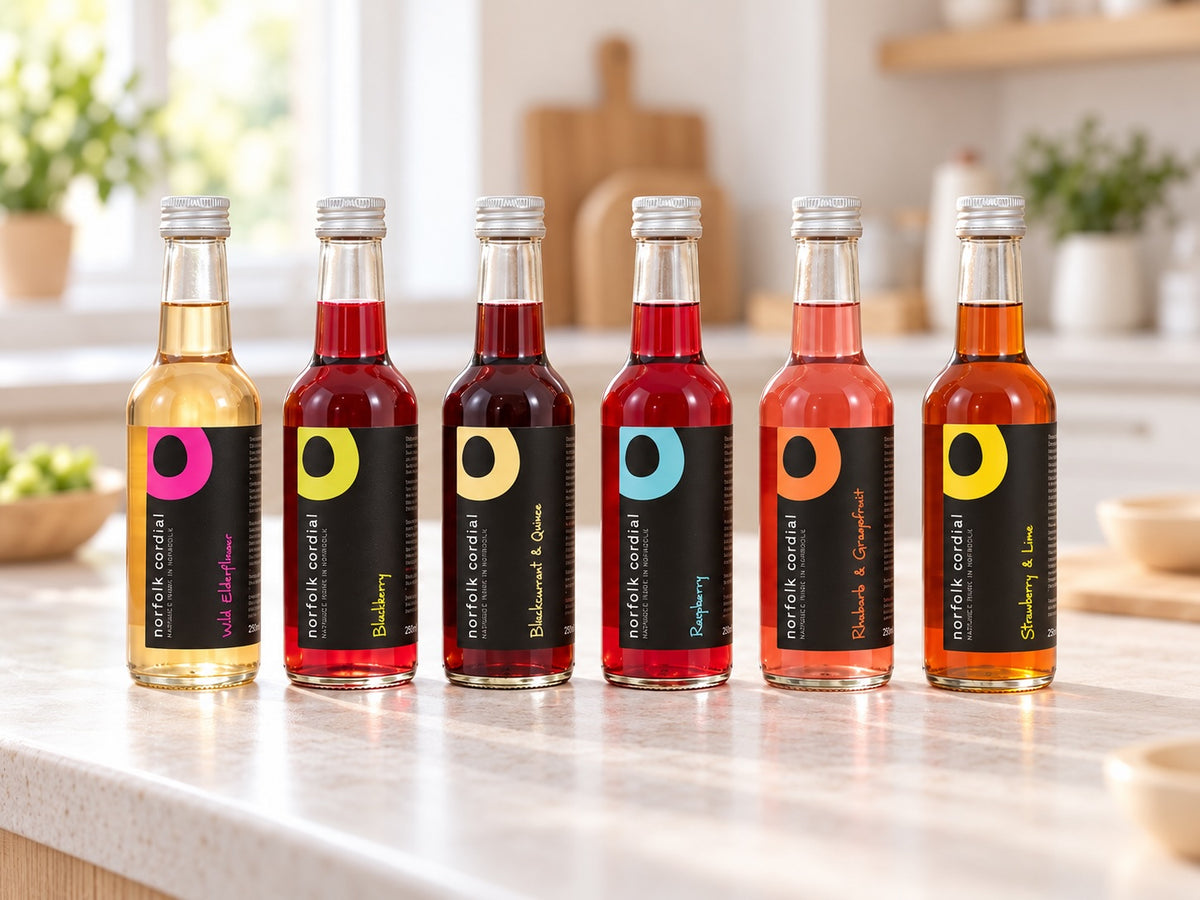 Six 250ml Norfolk Cordial bottles in assorted flavours arranged on a pale stone worktop in a bright contemporary kitchen.