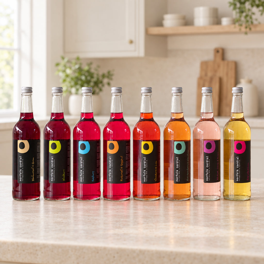 Eight 750ml Norfolk Cordial bottles in a bright contemporary kitchen, showing a colourful range of handcrafted fruit cordials.