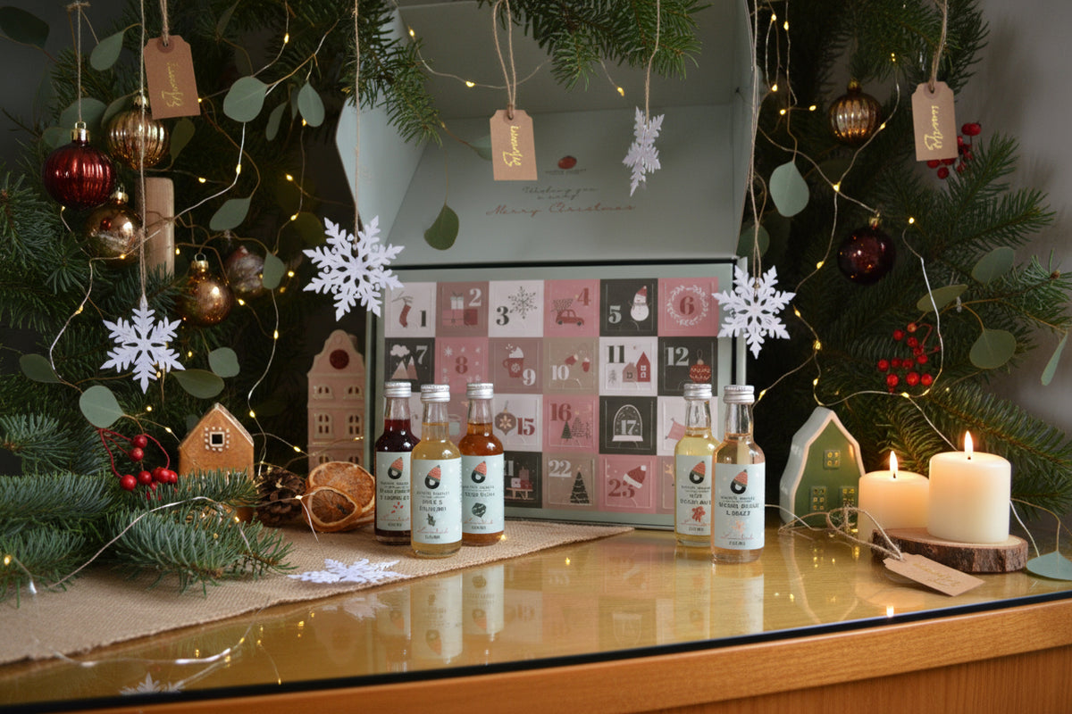Open Norfolk Cordial Christmas advent calendar showing 24 numbered doors, surrounded by individual mini cordial bottles, Christmas decorations and fairy lights.
