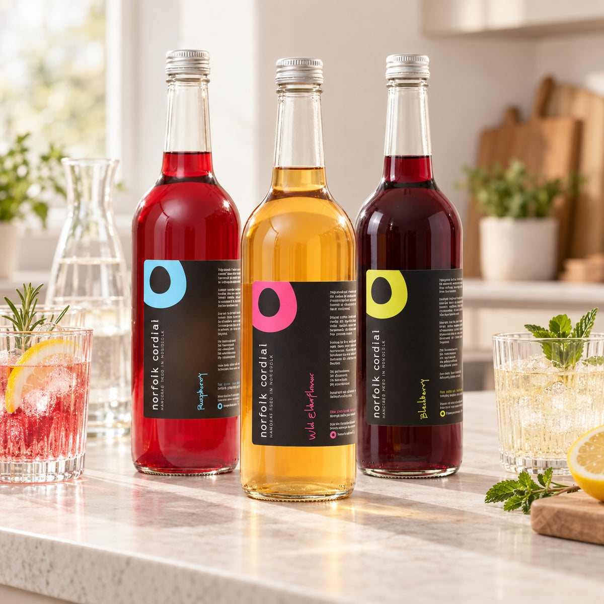 Three 750ml Norfolk Cordial bottles in Raspberry, Wild Elderflower and Blackberry displayed together in a bright contemporary kitchen as a mix-and-match multi-buy selection.